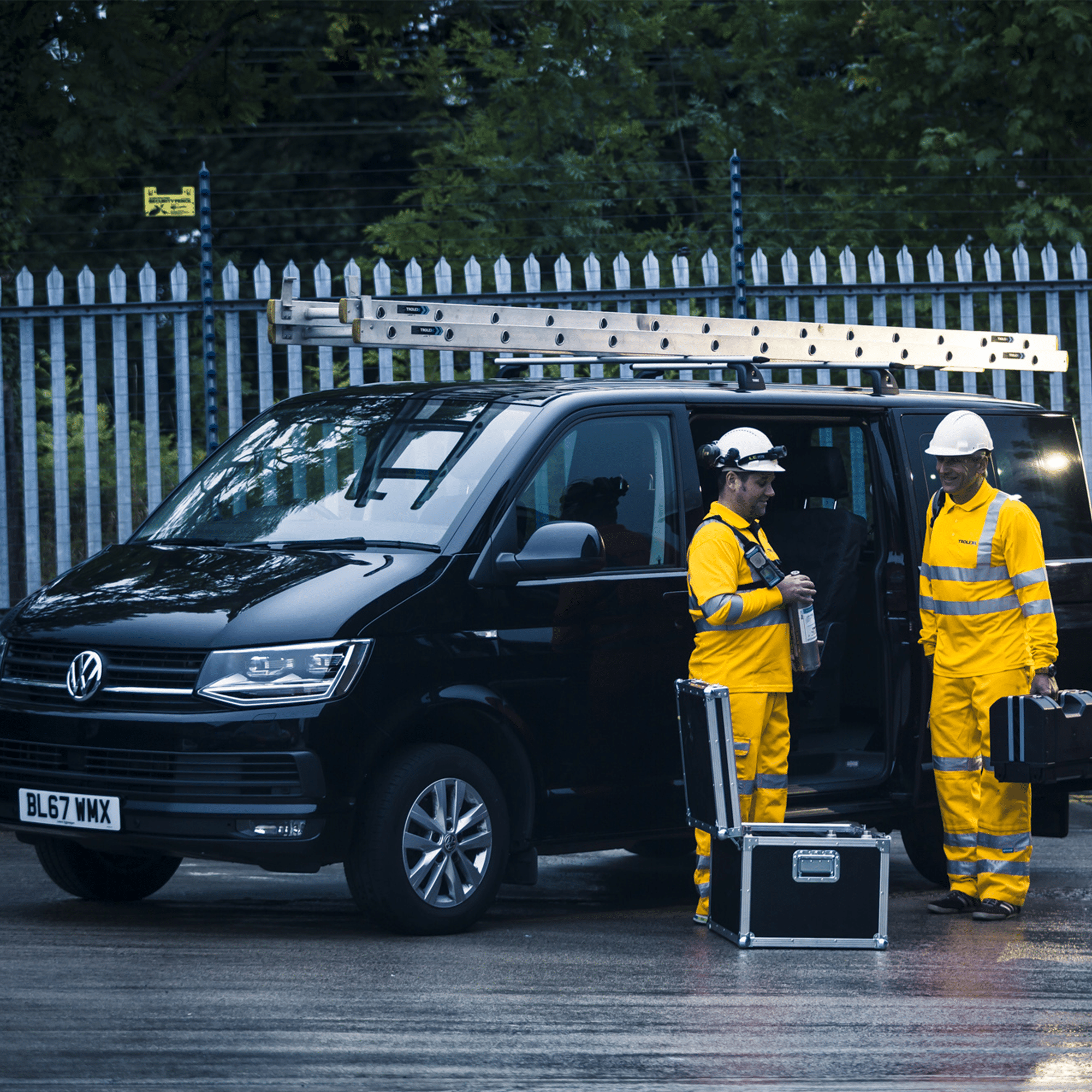 Two men in high-vis overalls standing in front of a van